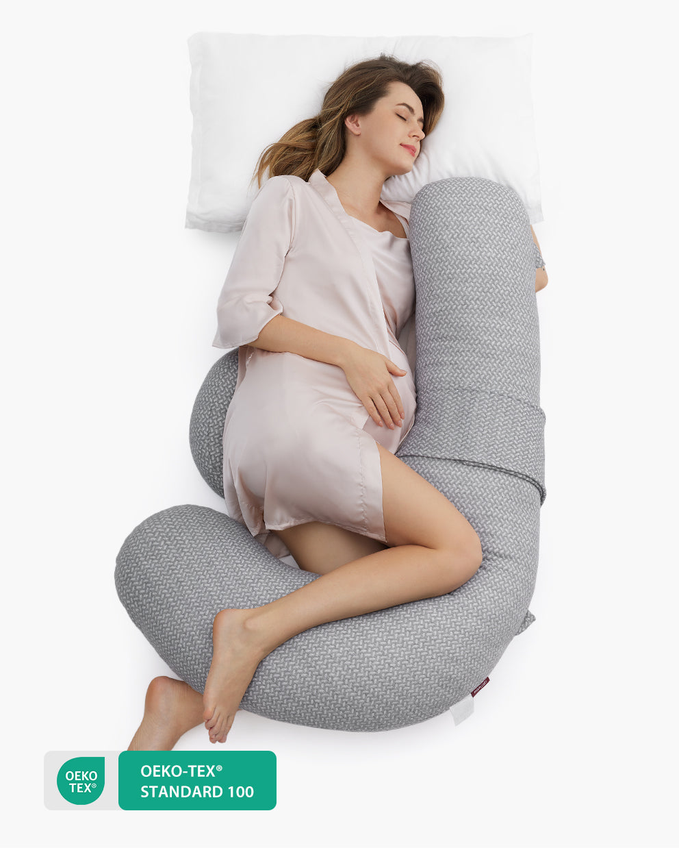 Pregnant woman sleeping soundly on a gray F-shaped Momcozy pregnancy pillow for full body support.